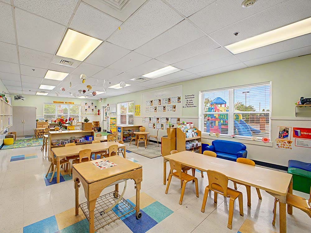 A classroom with small tables and chairs, and a playground visible through a window
