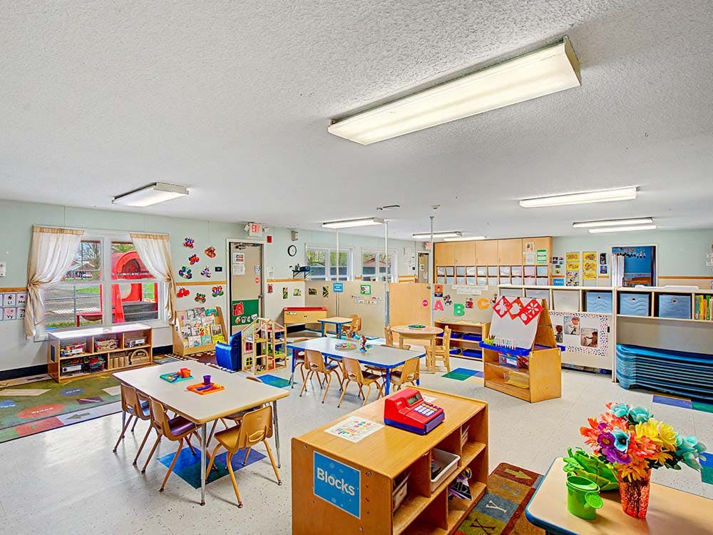 Empty kindergarten classroom with small tables, chairs, and learning materials