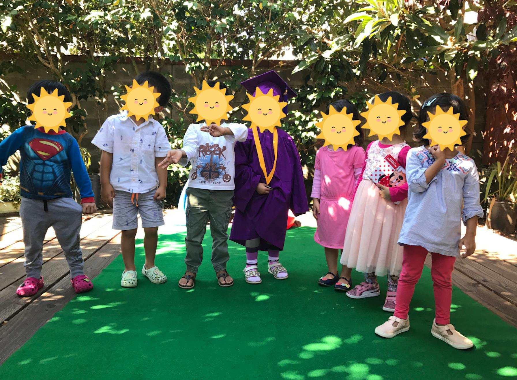 Group of children standing together on a green mat outdoors