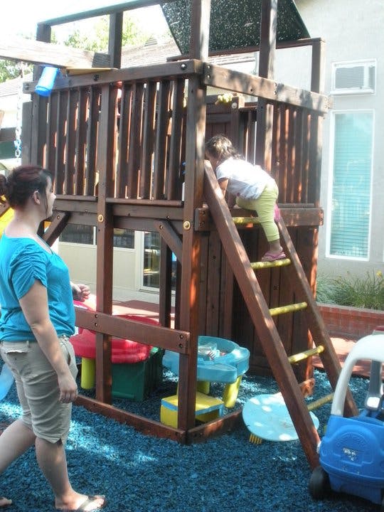 Person watching a child climb a ladder on a wooden play structure