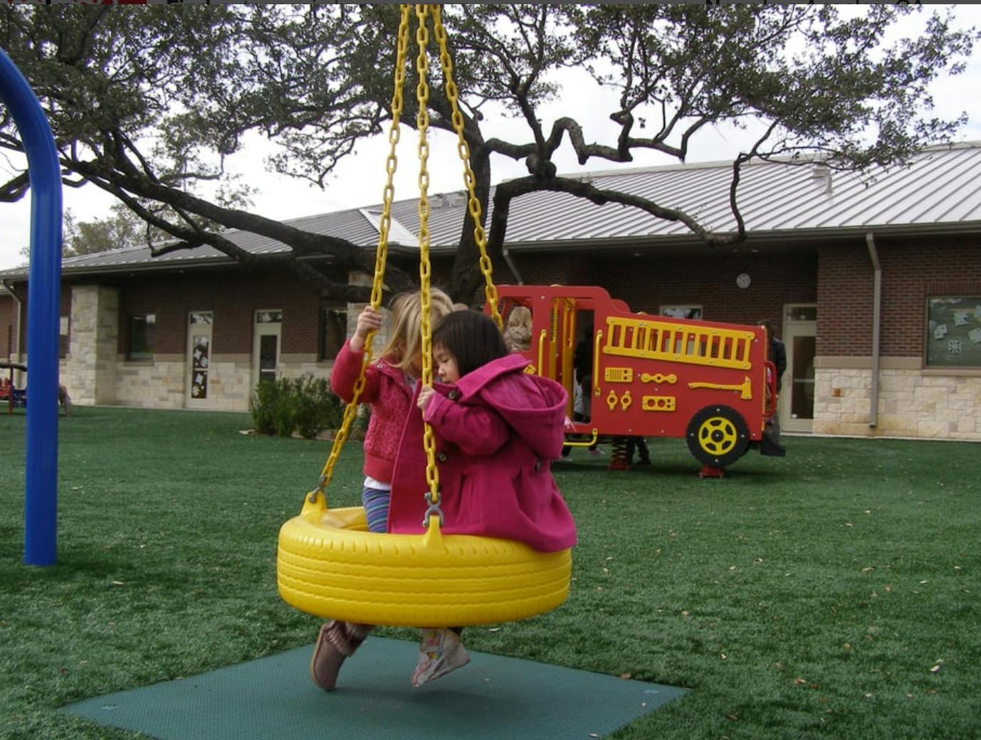 Two children on a yellow tire swing on a playground