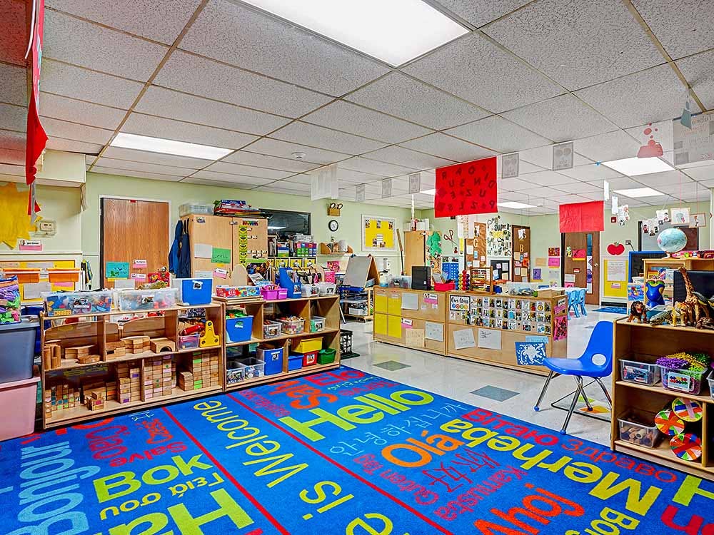 Classroom with children's toys and learning materials on shelves and a blue rug