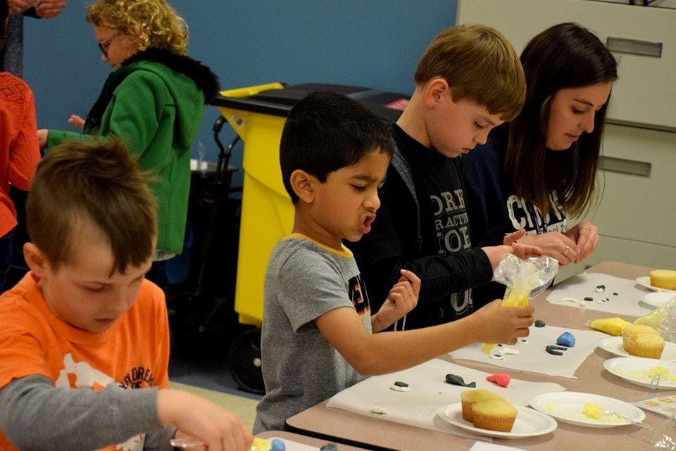 Children and a person decorating cupcakes at a table