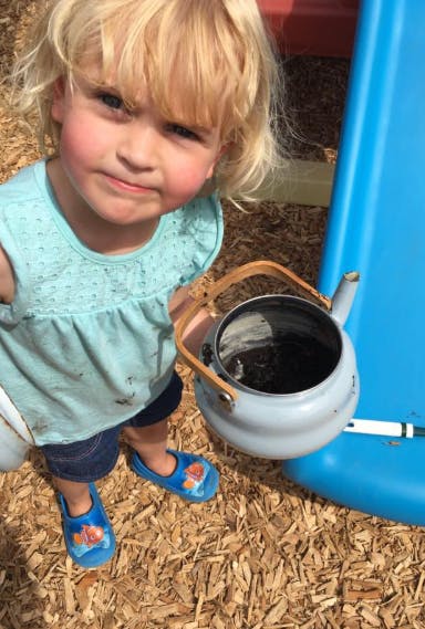 Child holding a kettle filled with dirt