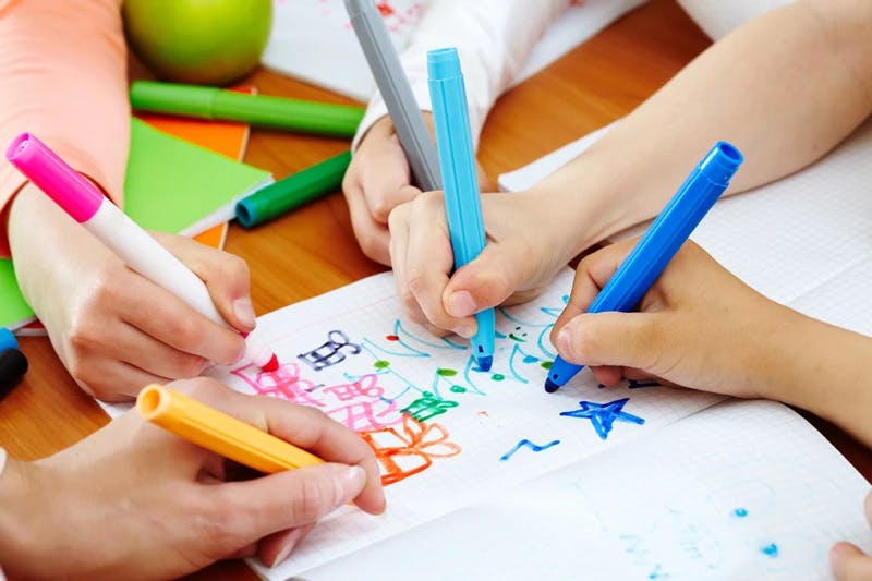 Multiple children drawing on paper with markers