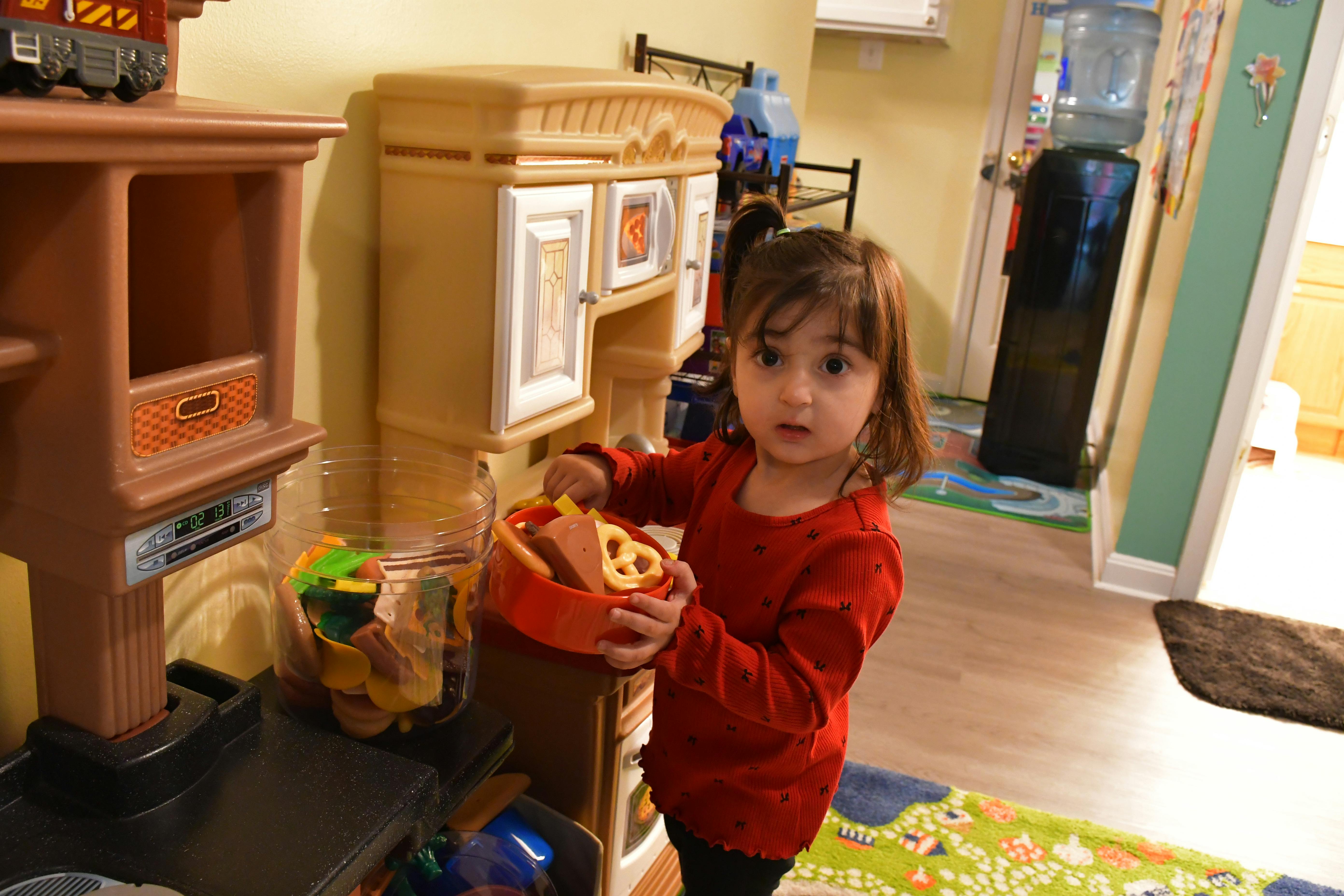 Child holding a toy basket with play food in a play kitchen