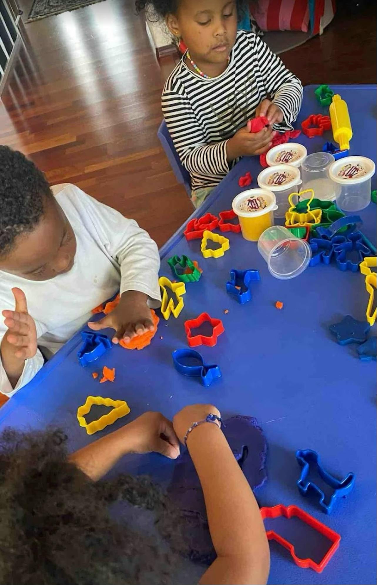 Three children playing with play-doh and cookie cutters at a blue table