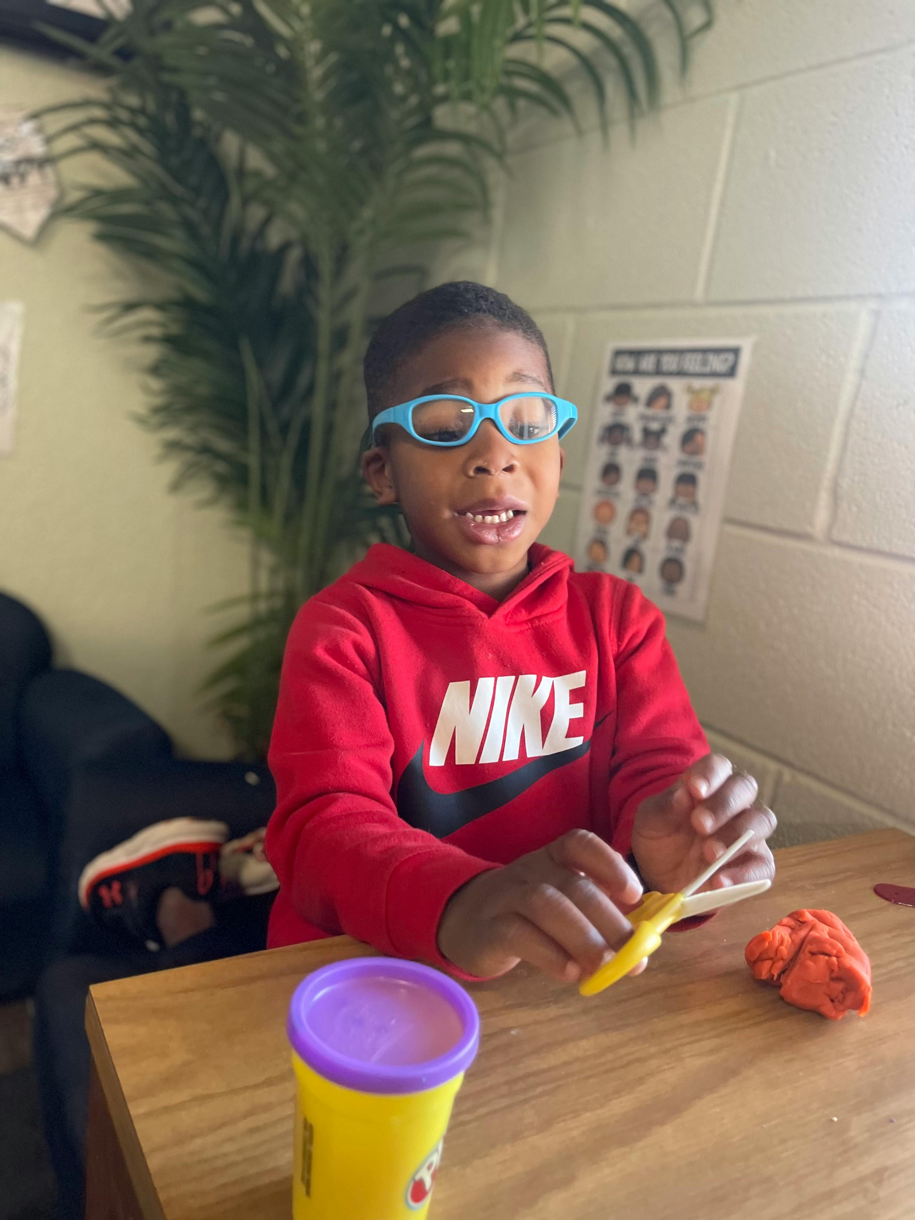 Child in blue glasses and red sweatshirt playing with modeling clay