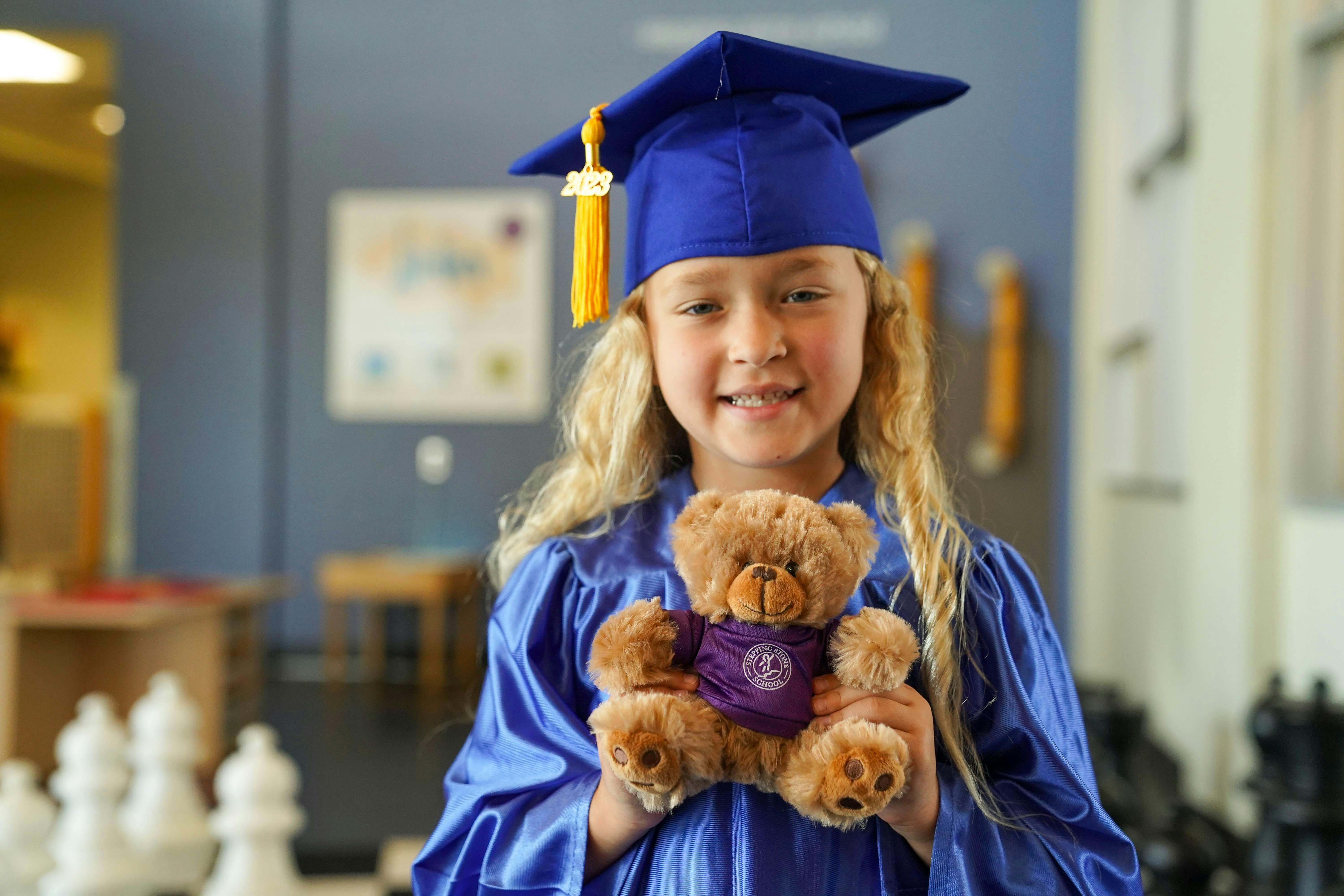 Child in graduation cap and gown holding a teddy bear