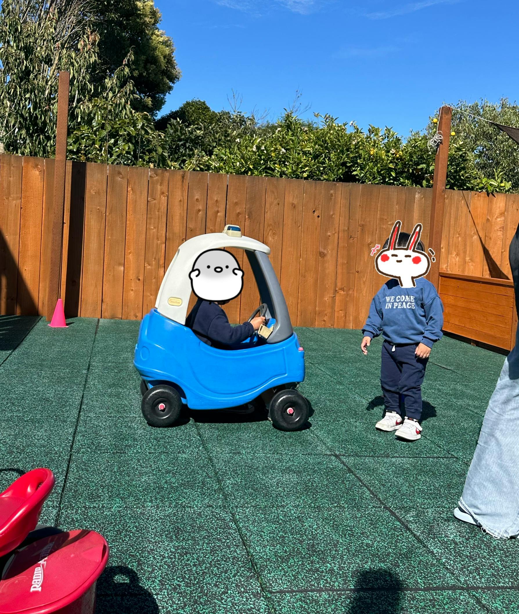 Child in a toy car with another child standing nearby on a playground
