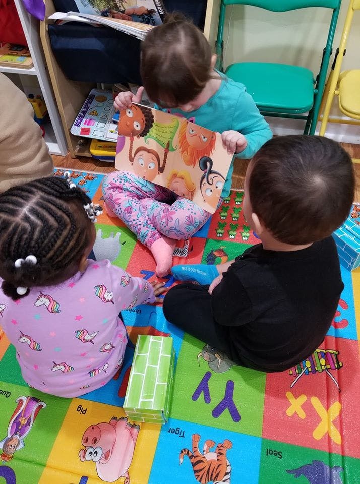 Three children sitting on a mat, one child holding an open book