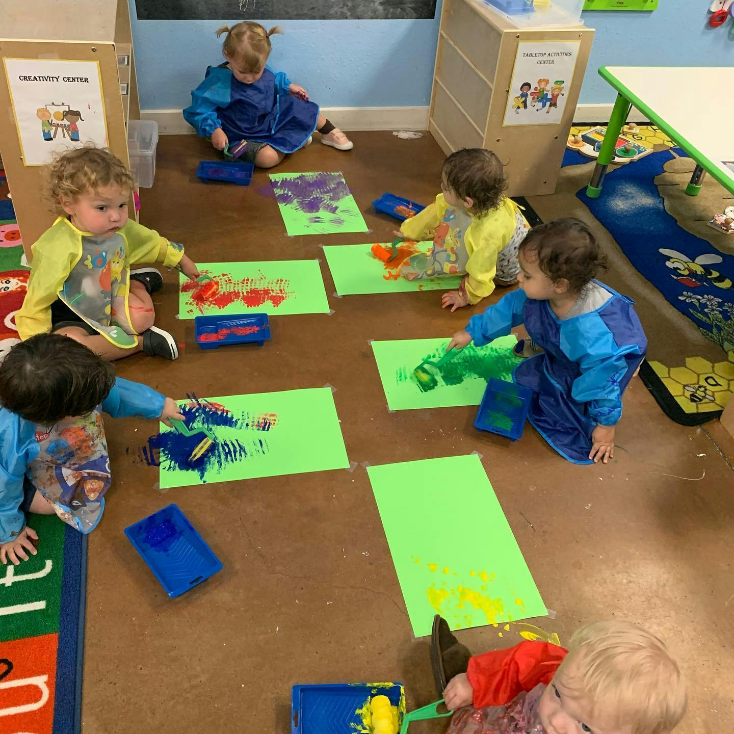 Children finger painting on paper on the floor