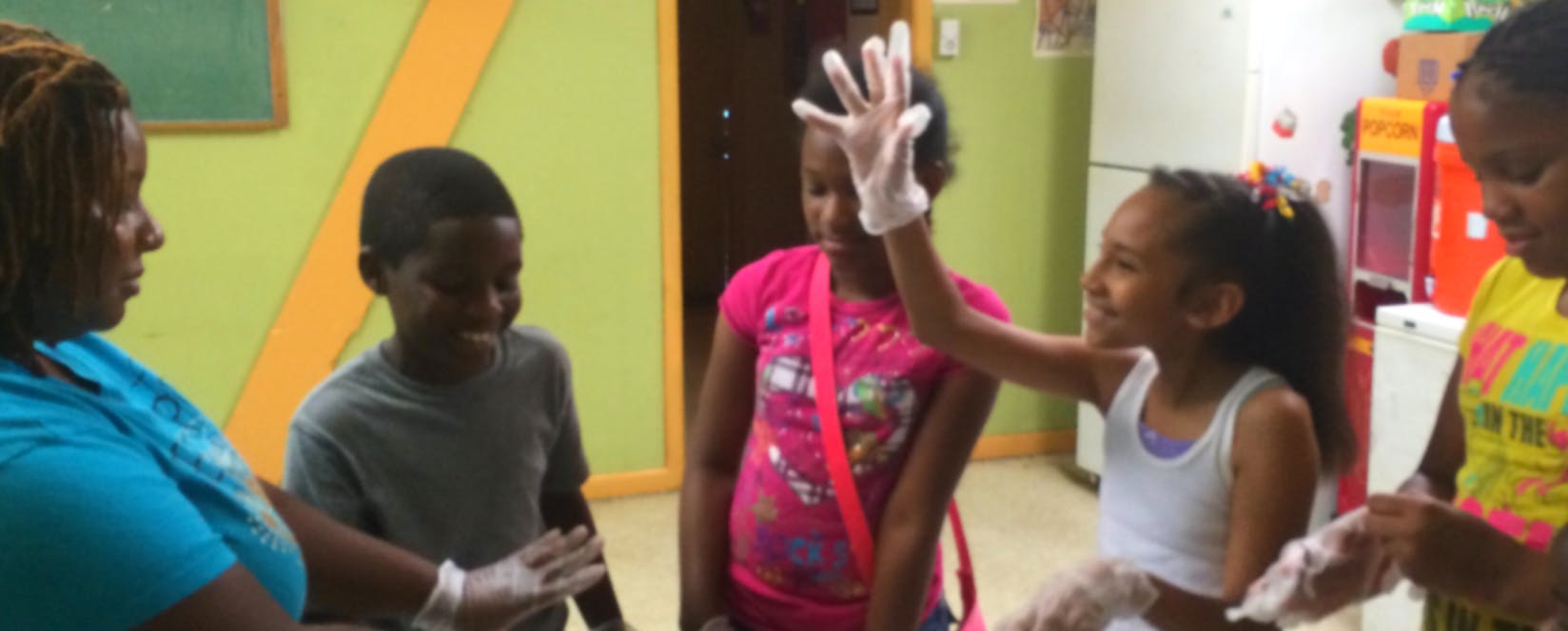 Adult and children wearing gloves, one child raising a hand