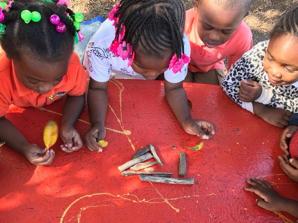 Four children looking down at sticks and leaves on a red surface