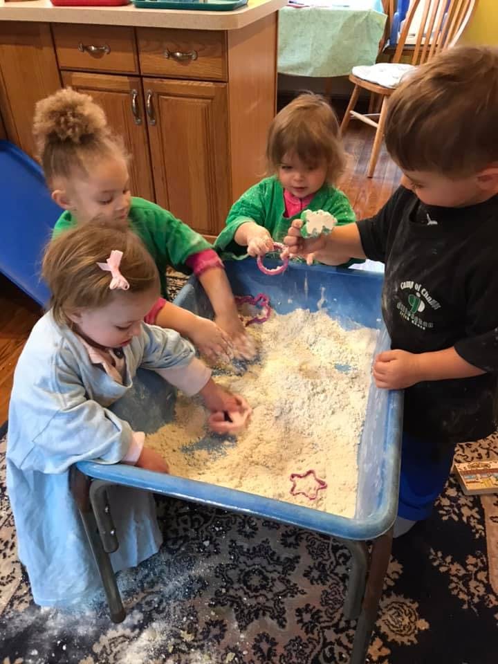 Children playing with flour and cookie cutters in a blue bin