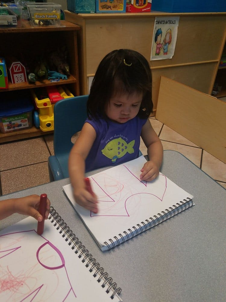 Child drawing with a red crayon in a notebook