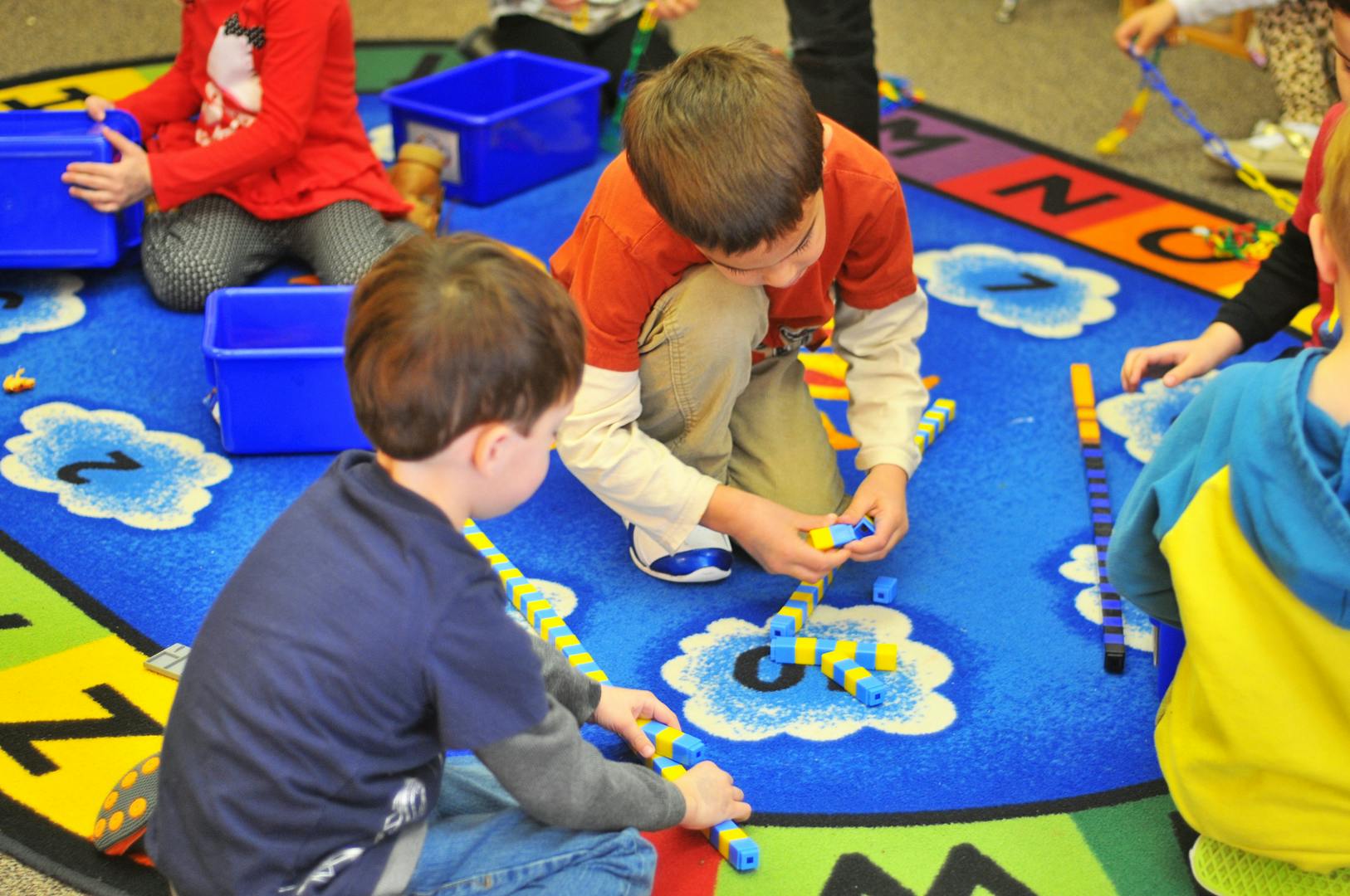 Children playing with building blocks on a colorful rug in a classroom