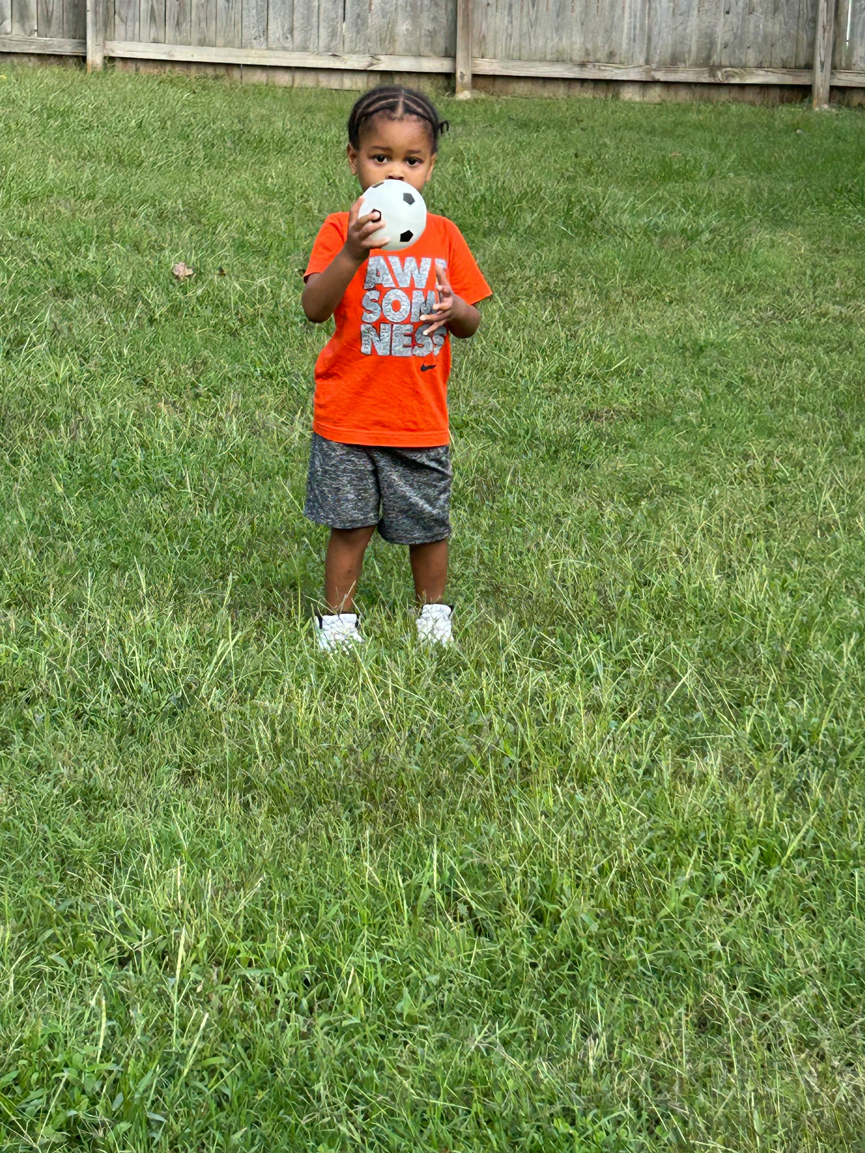 Child holding a small soccer ball in a grassy area