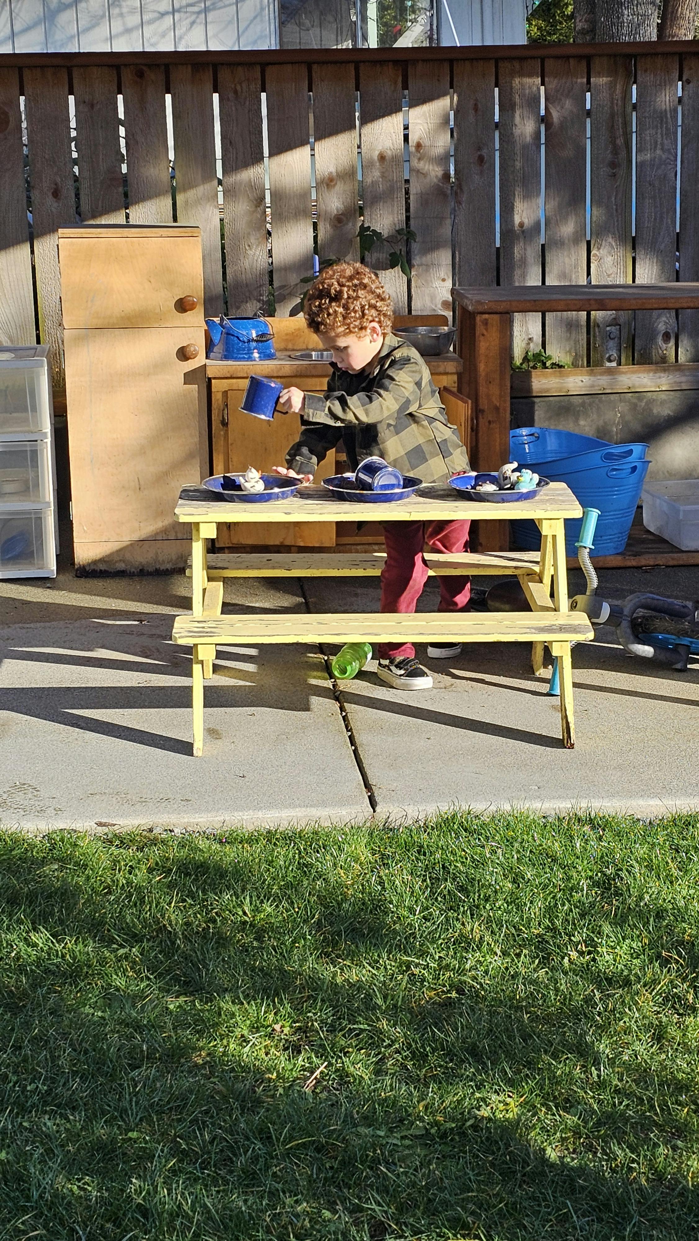 Child playing with cups and plates at a small picnic table