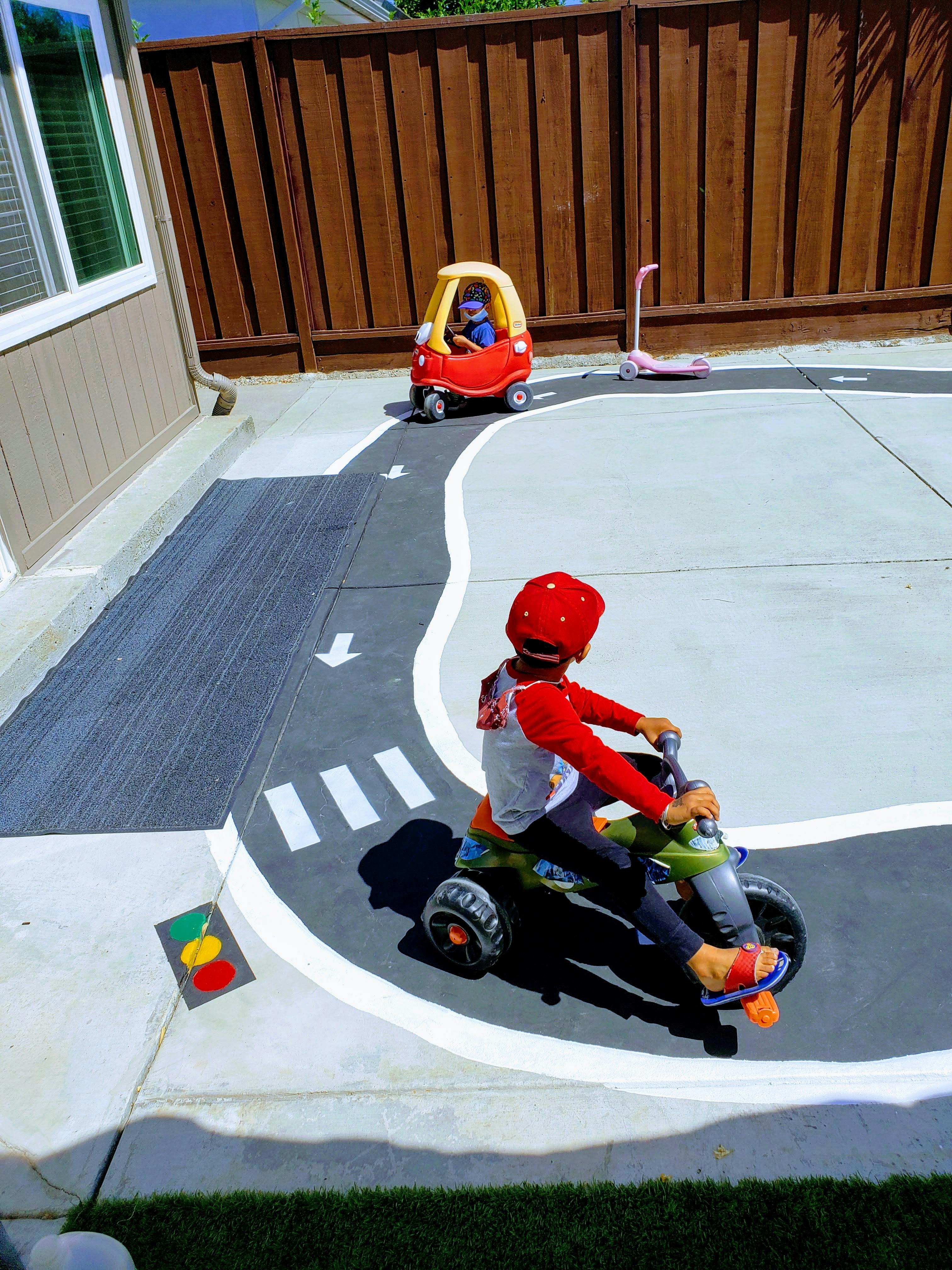 Child on a tricycle and another child in a toy car on a painted road