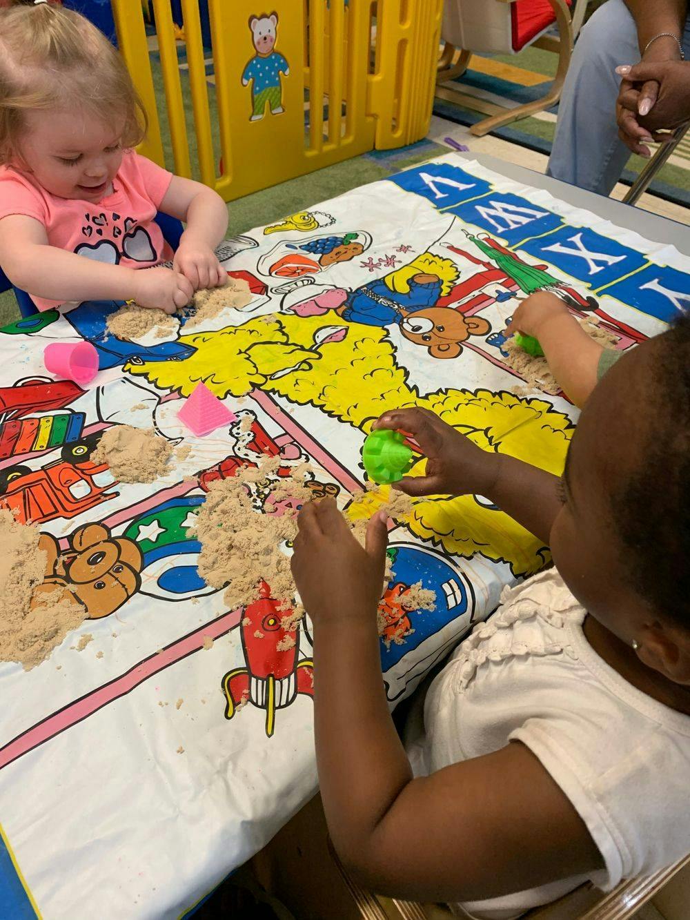 Two children playing with kinetic sand on a colorful mat