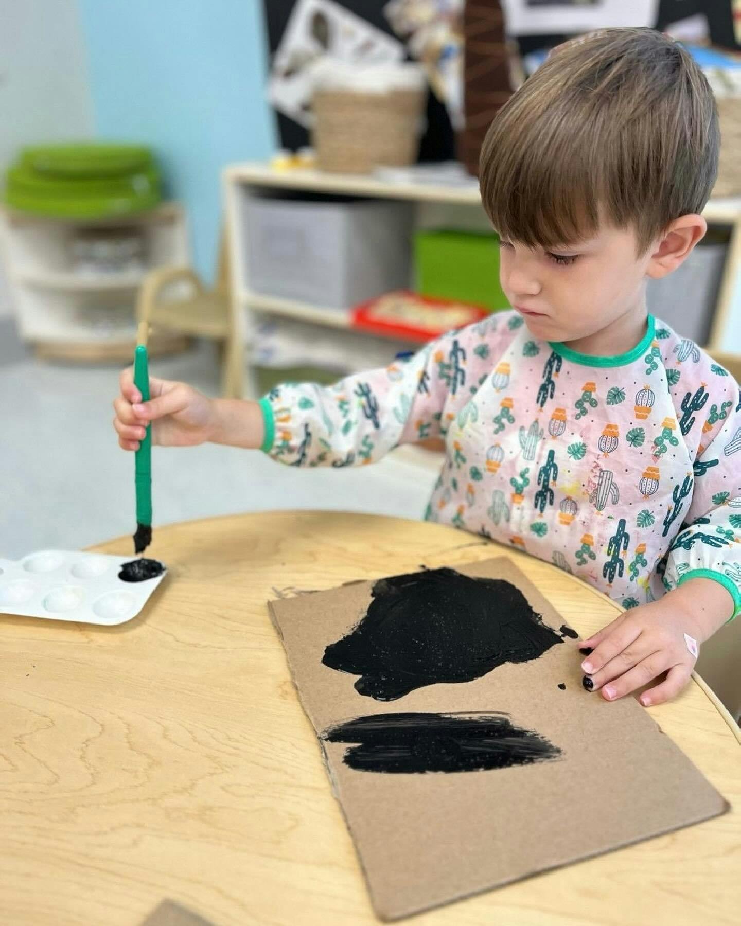 Child painting with black paint on cardboard