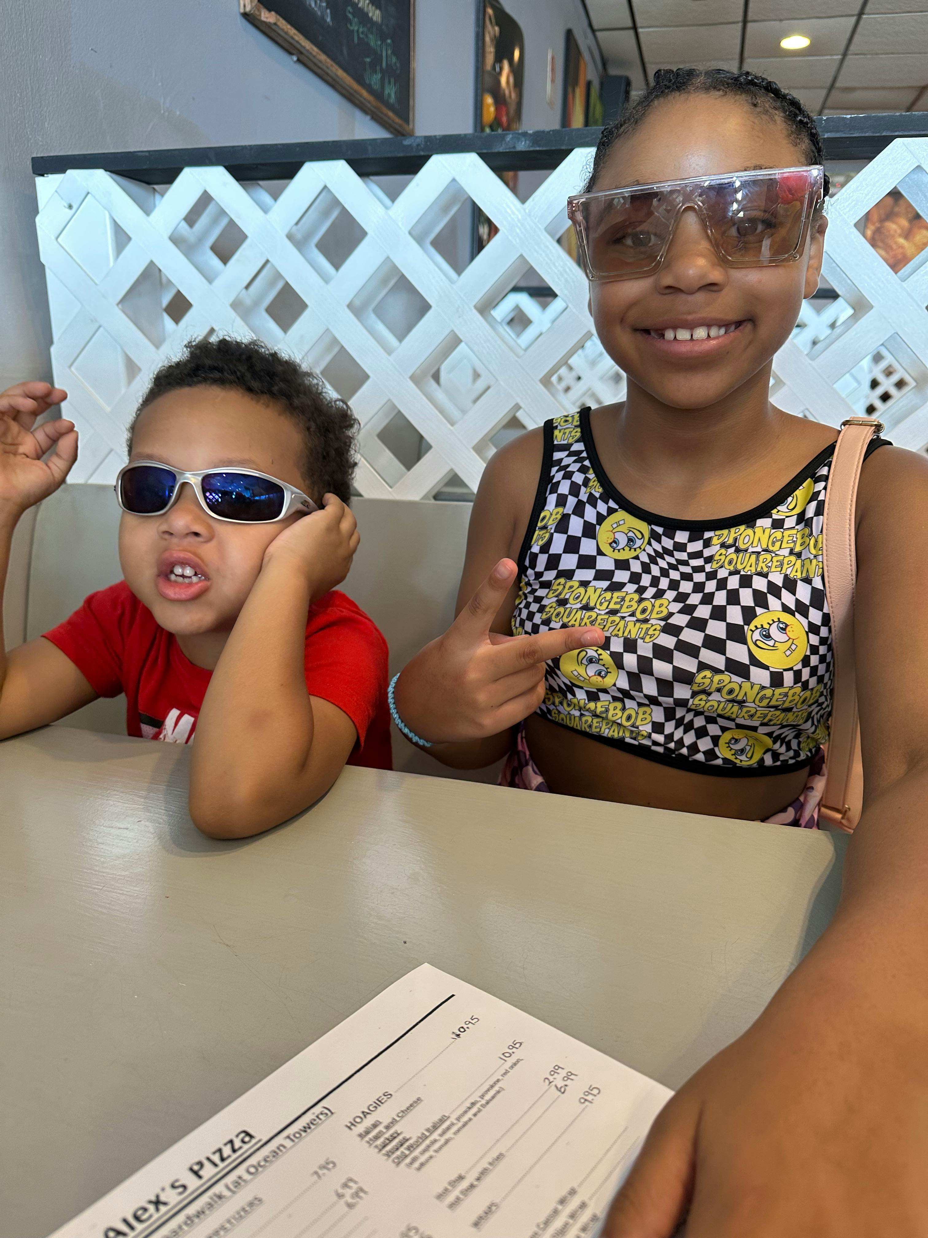 Two children wearing sunglasses sitting at a table, one pointing