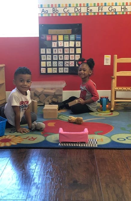 Two children playing with blocks on a colorful rug in a classroom