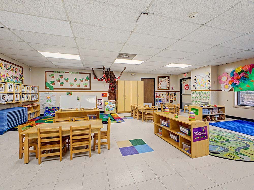 Classroom with small wooden tables and chairs, shelves, and colorful decorations