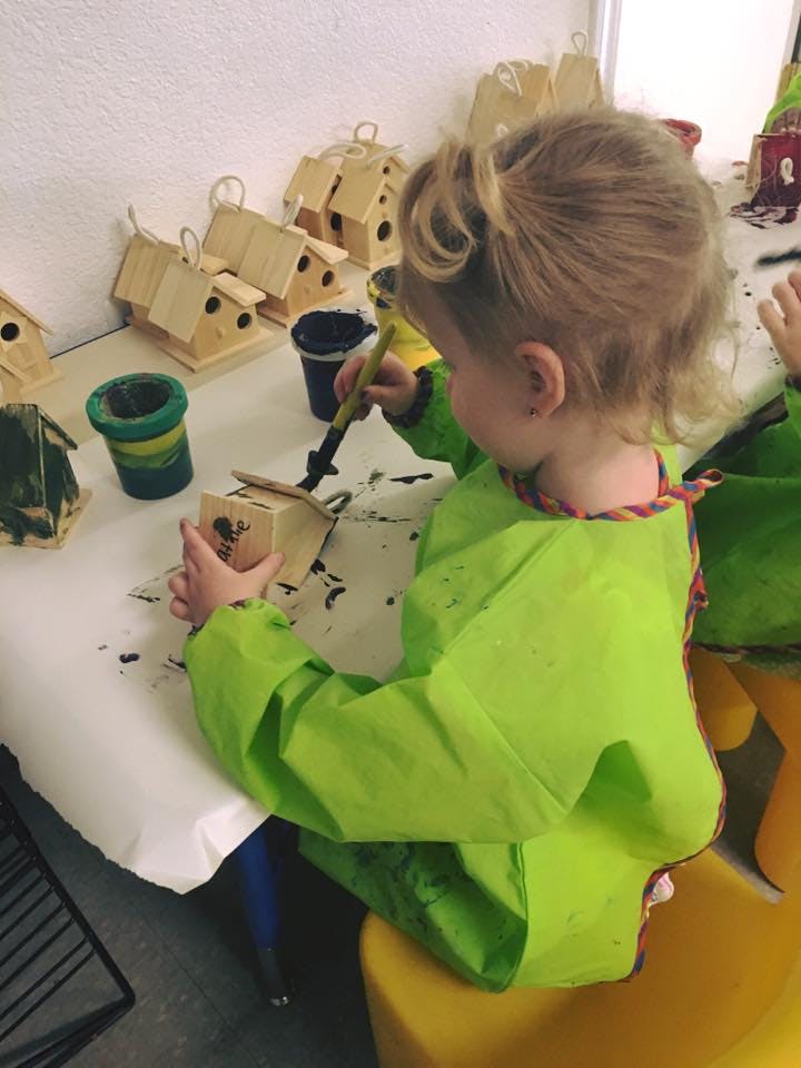 Child in a green smock painting a small wooden birdhouse