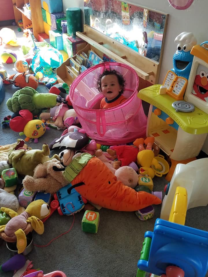 Child sitting in a pink mesh pop-up hamper surrounded by toys