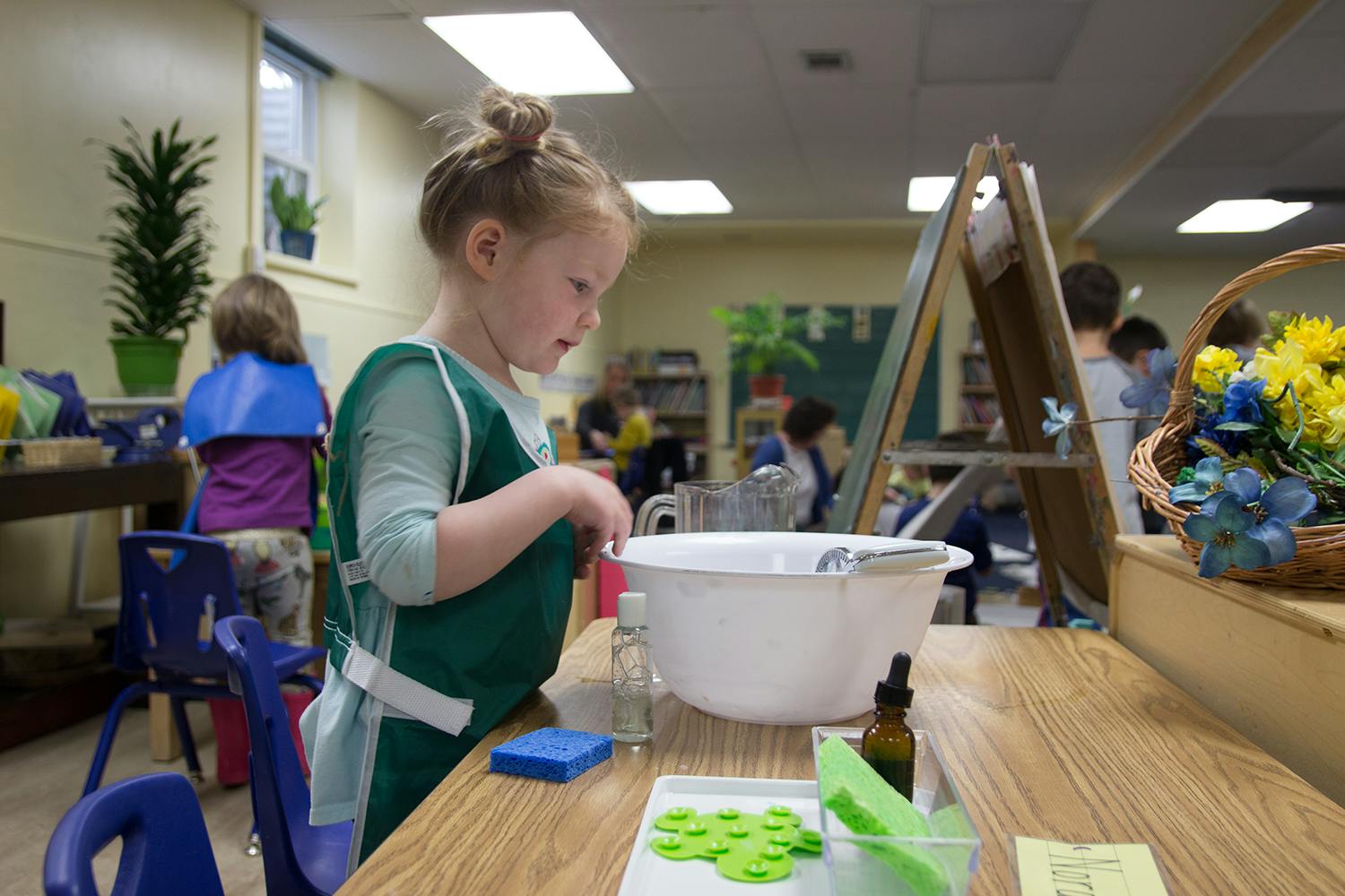 Child in a classroom standing at a table with a bowl