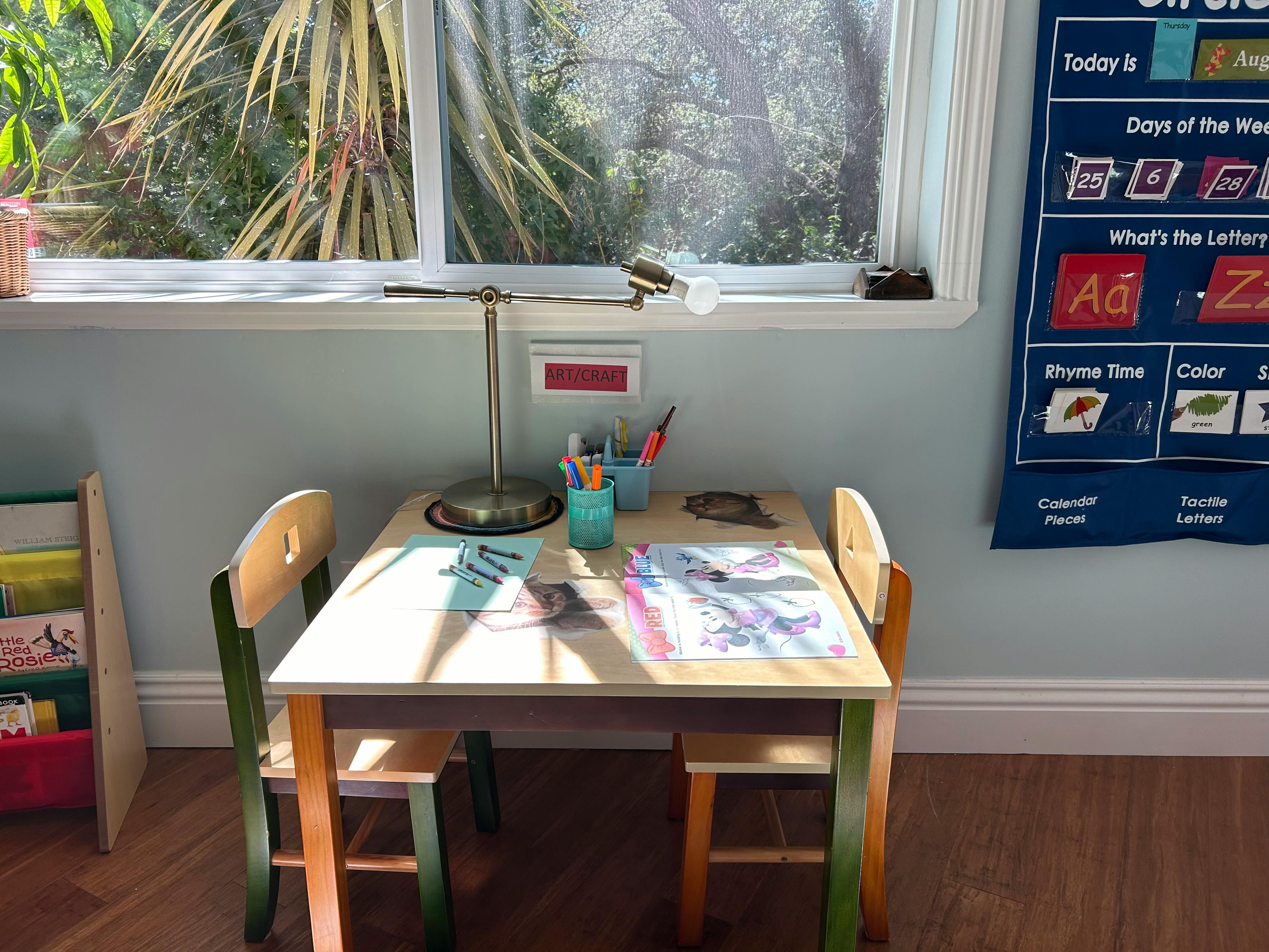 Child's desk with two chairs, a lamp, and papers near a window