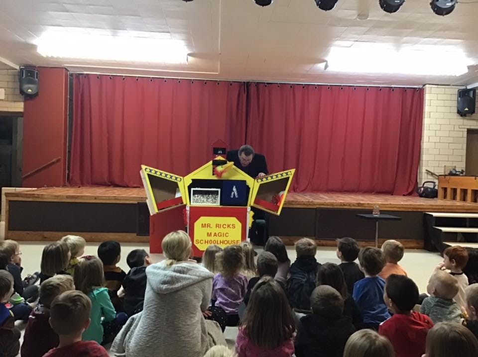 Person on stage with a prop, children watching from the floor
