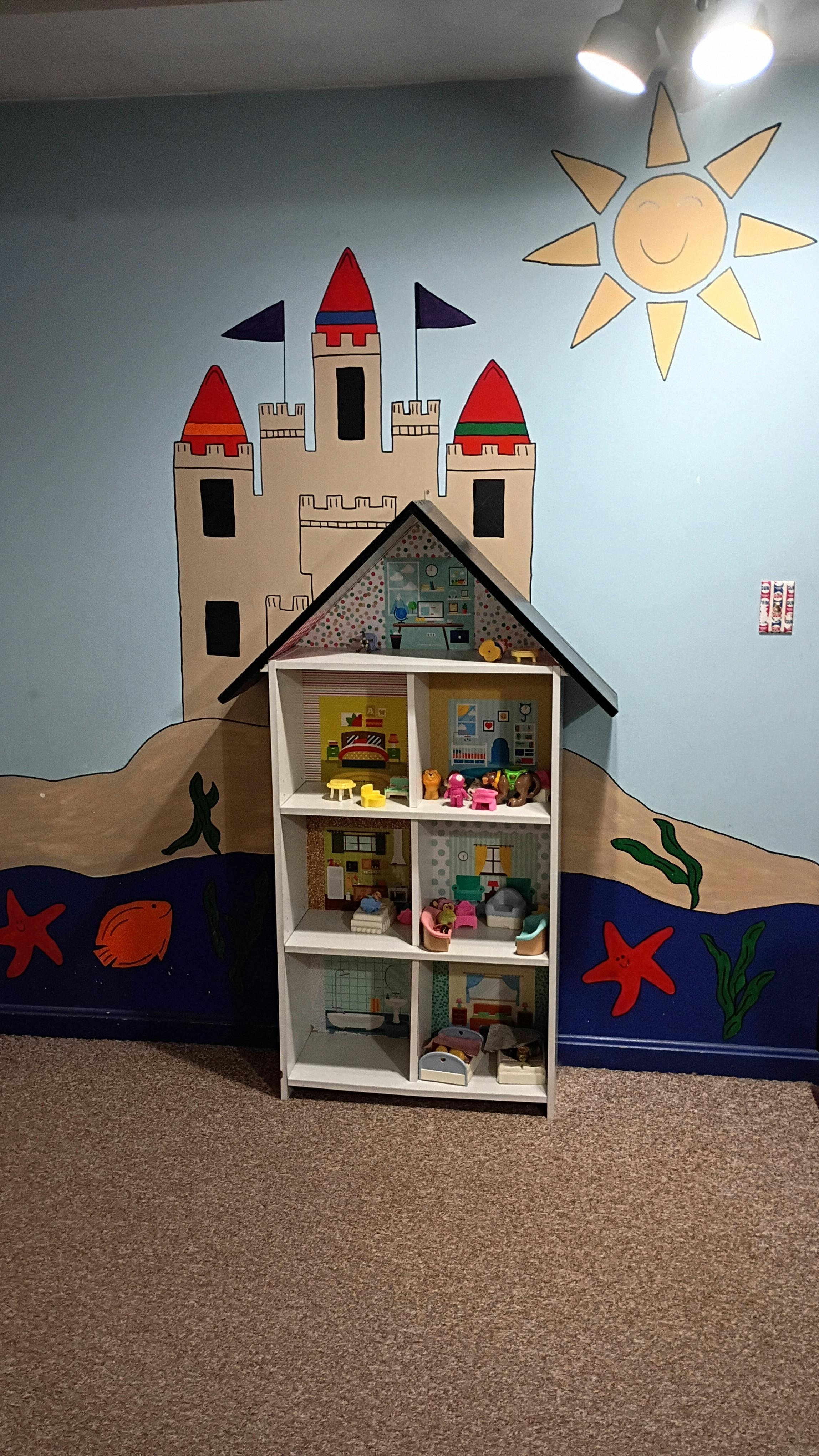Dollhouse placed against a wall painted with a castle and ocean theme