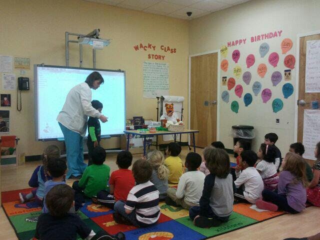 Adult and child at a whiteboard in a classroom with other children watching
