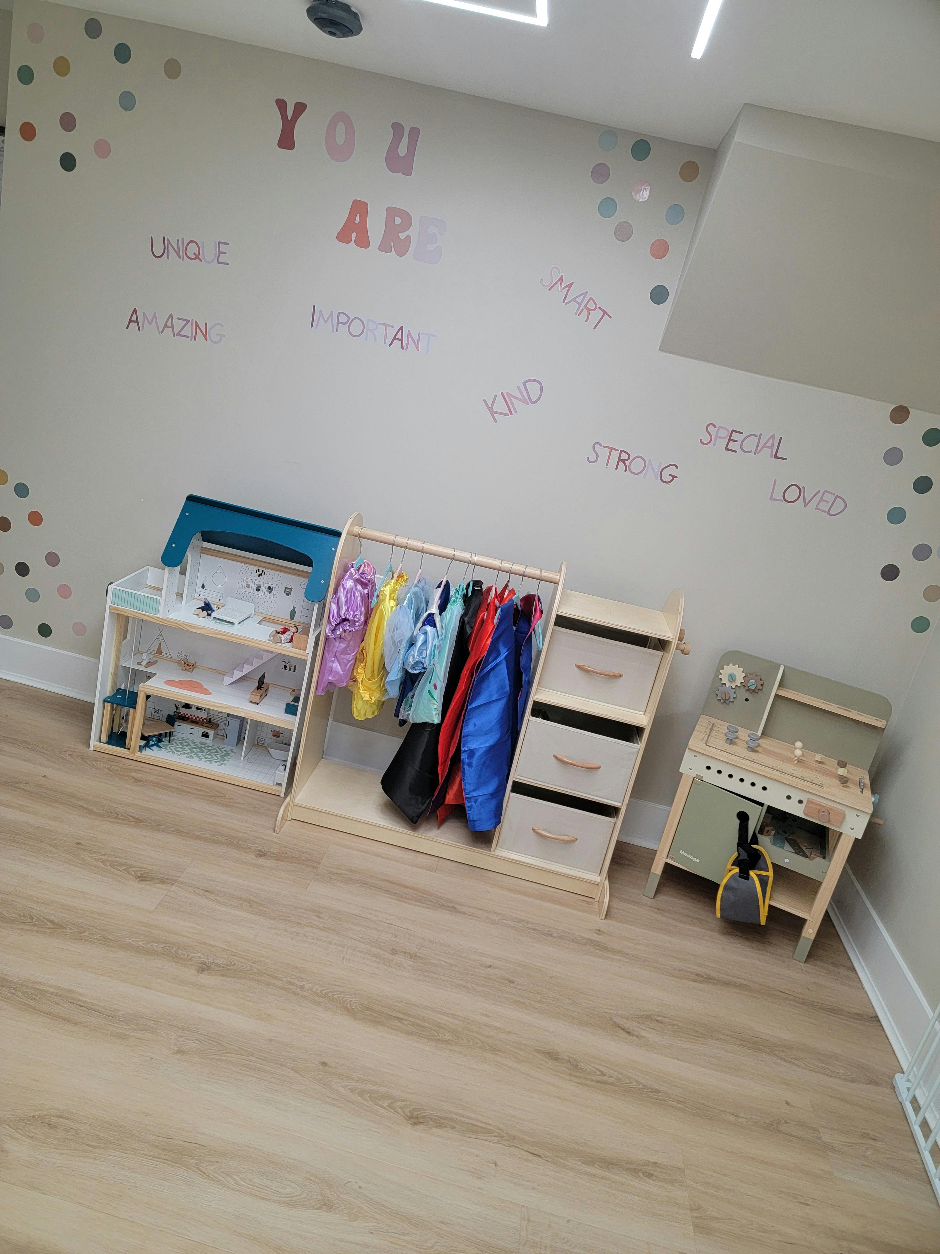 Children's play area with dress-up clothes, shelves, and a toy kitchen