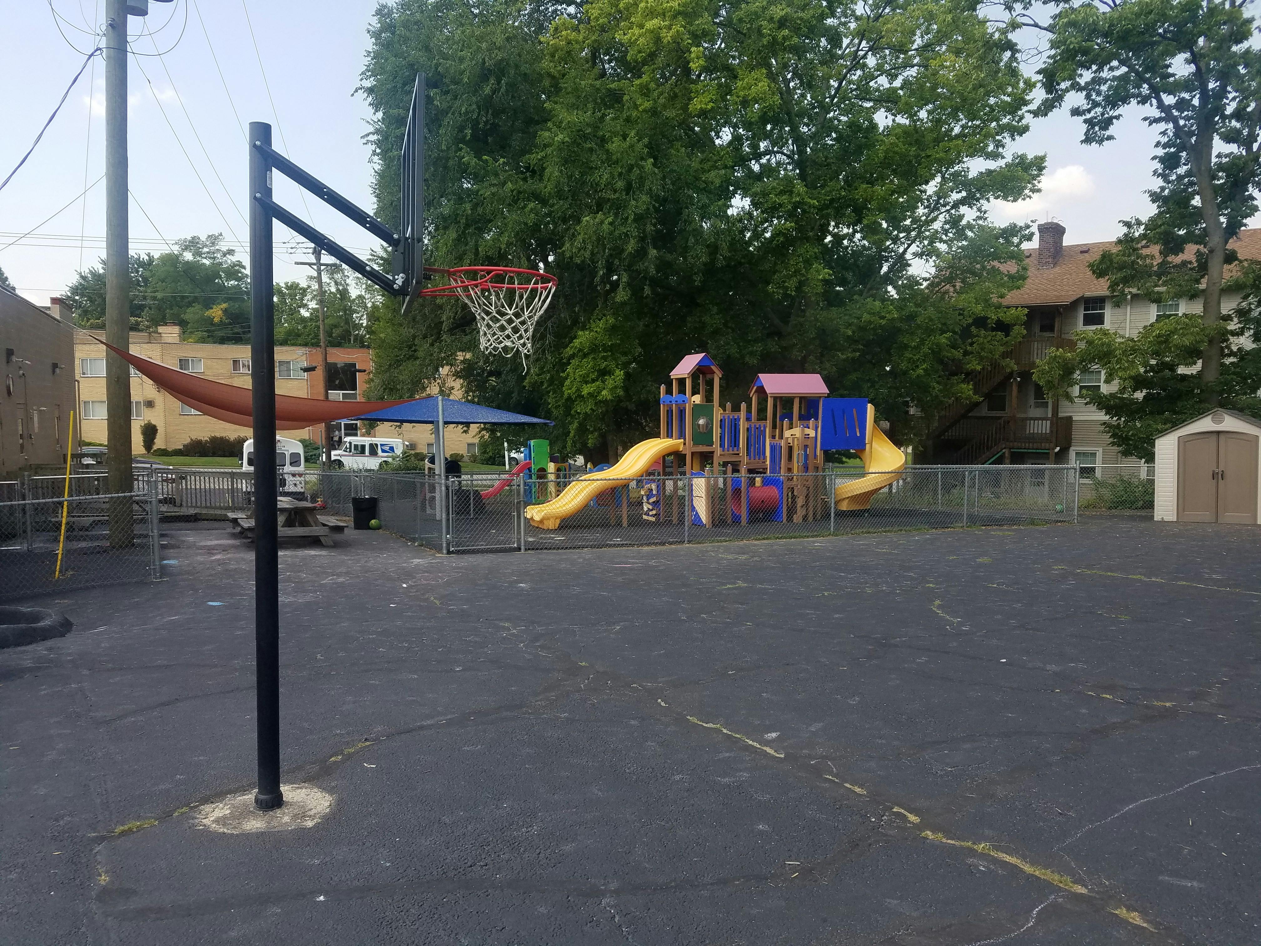 Basketball hoop on a paved court with a playground in the background