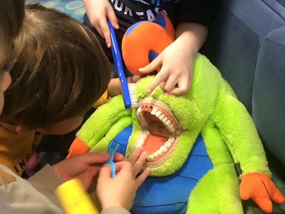 Children brushing the teeth of a large stuffed animal with a dental model mouth
