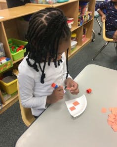 Child gluing paper shapes onto a paper plate