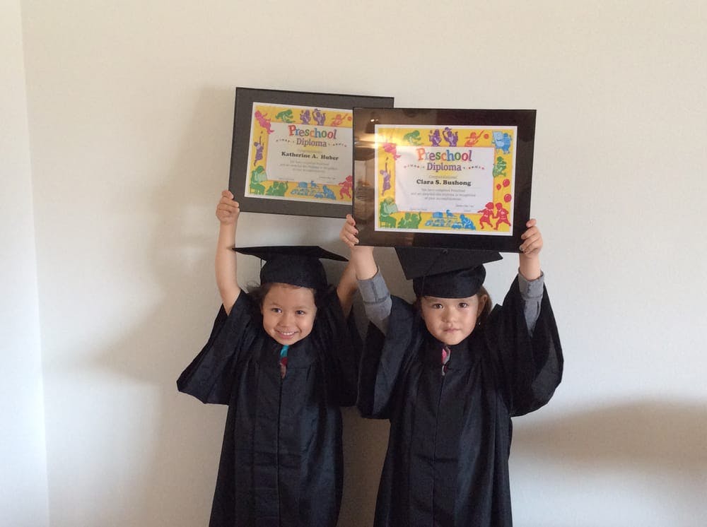 Two children in graduation caps and gowns holding up framed diplomas