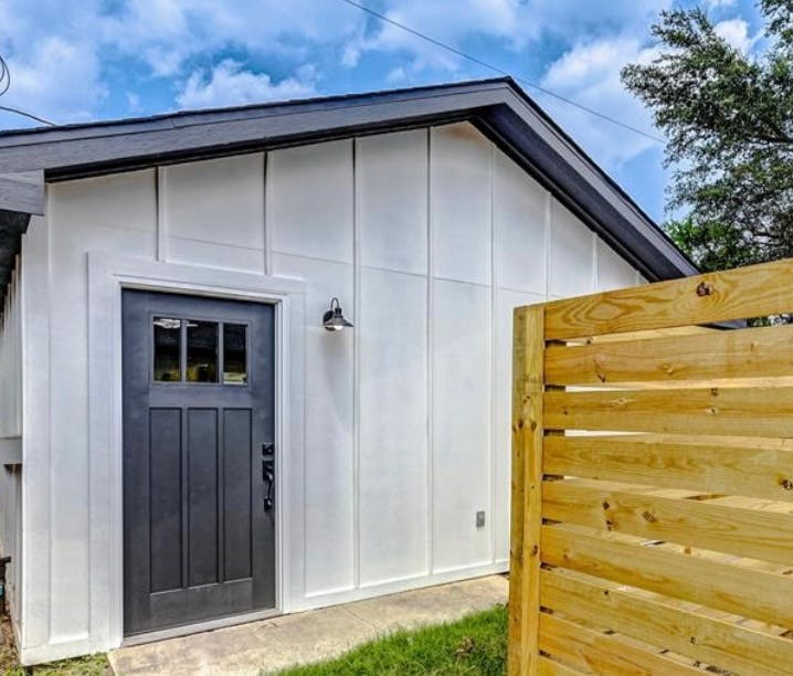 White building with a dark door and a wooden fence