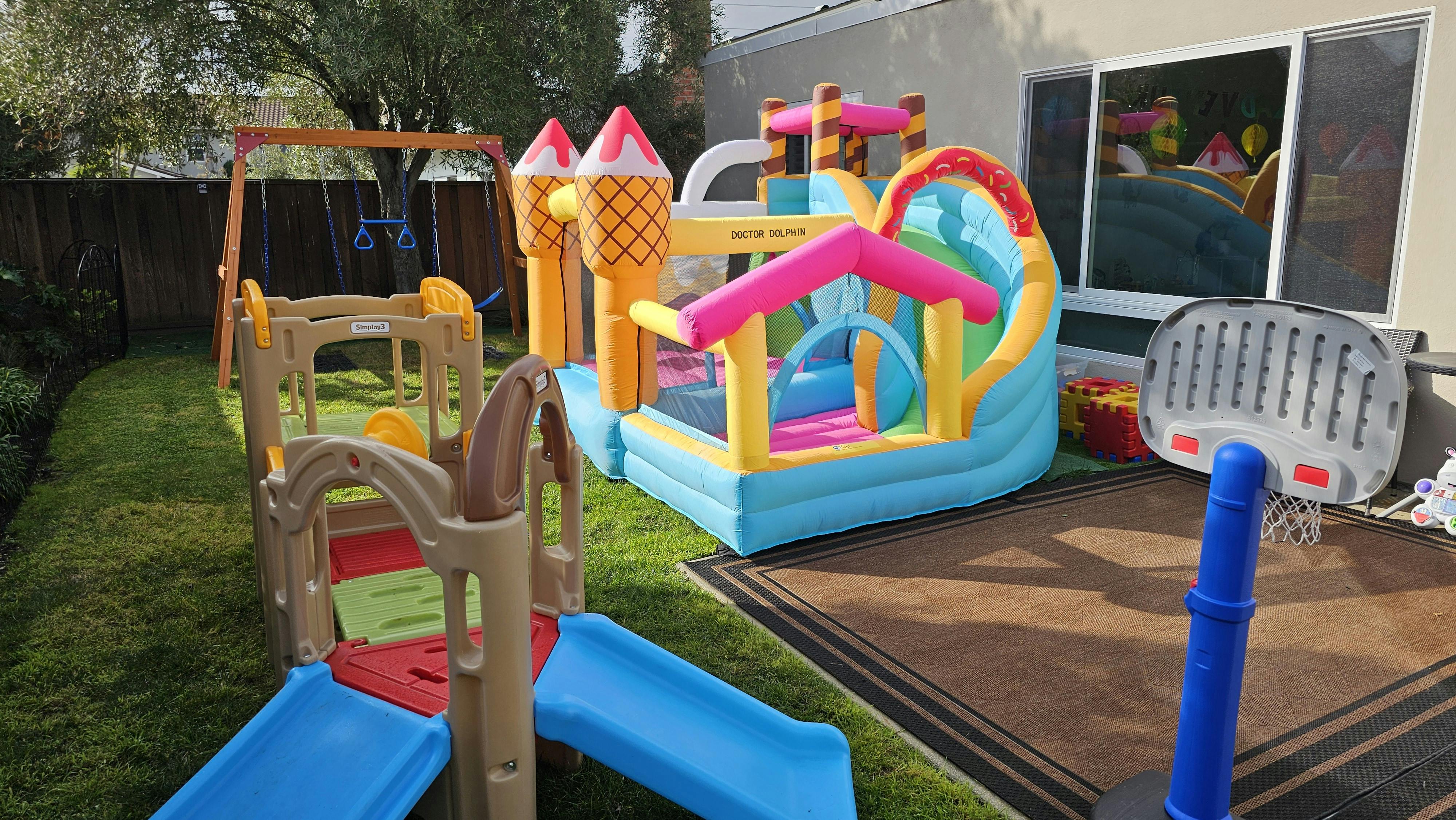 Outdoor play area with a bounce house, swing set, and slide