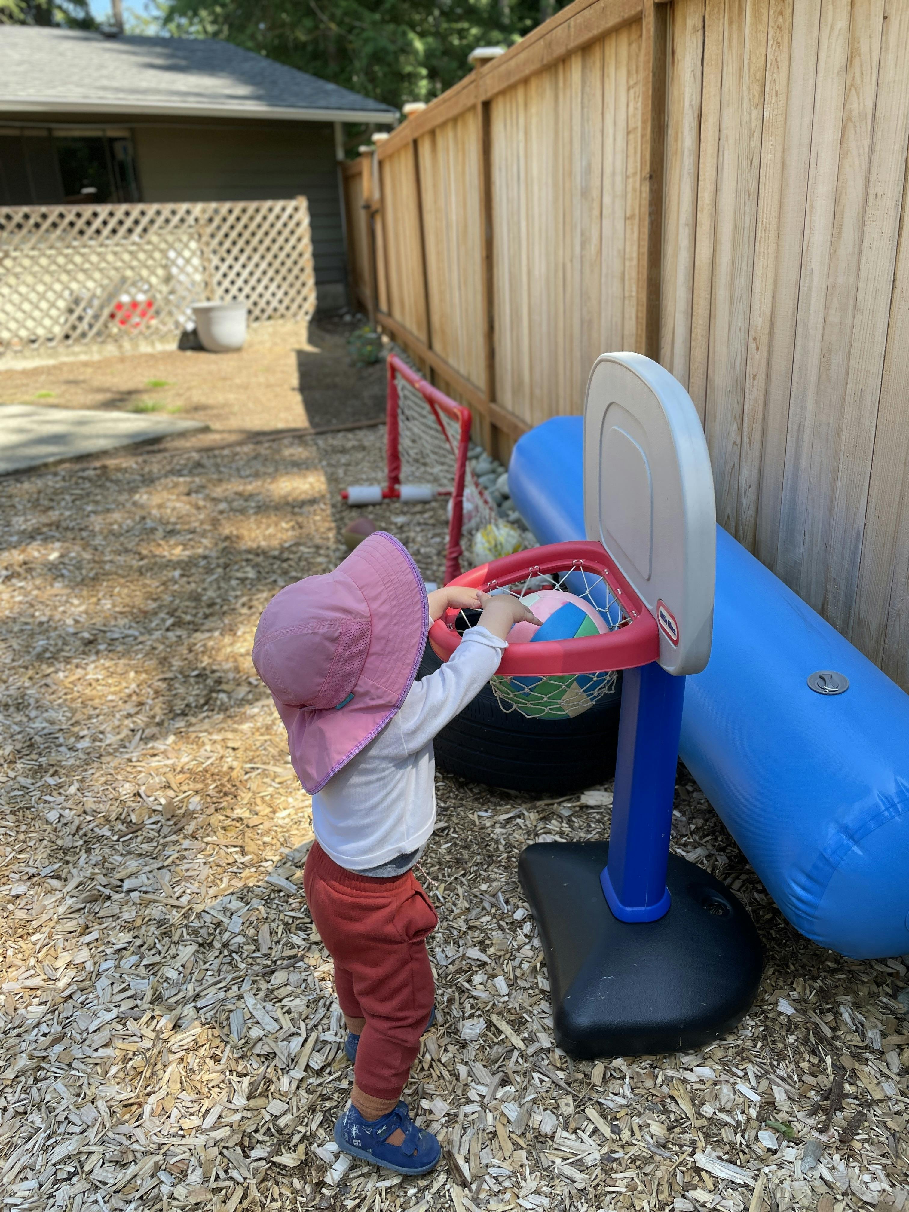 Child in a pink hat playing with a toy basketball hoop