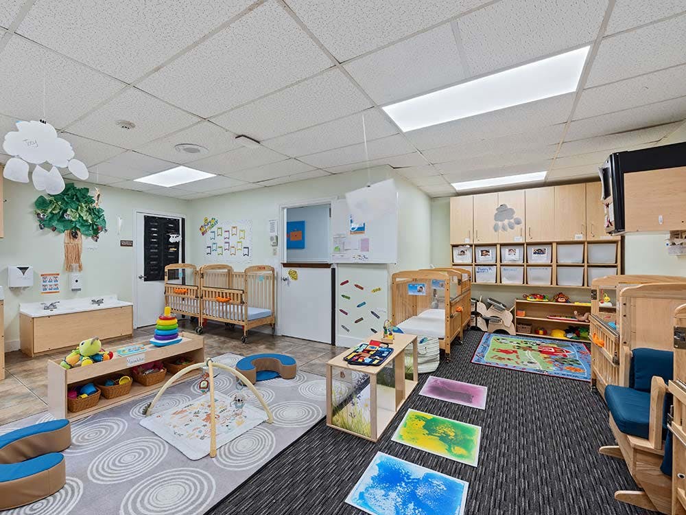 A colorful daycare room with cribs, play mats, and learning materials