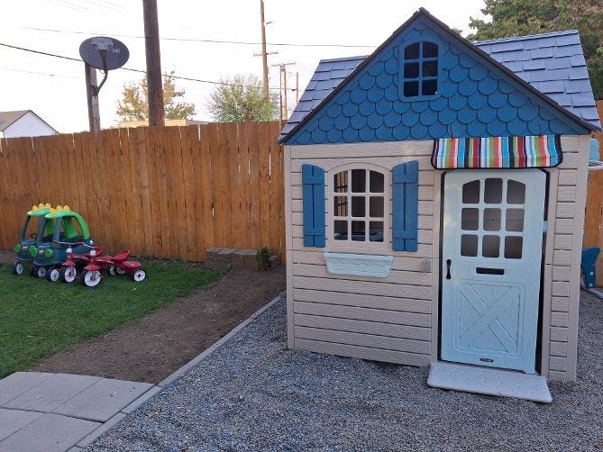 Plastic playhouse with ride-on toys on a backyard lawn