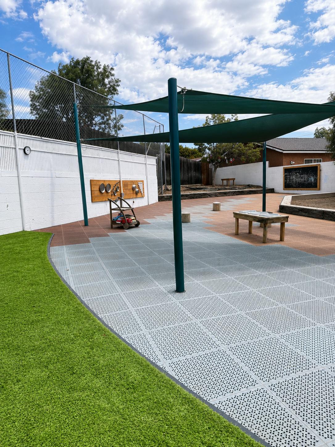 Outdoor children play area with artificial turf, tile flooring, and shade sails