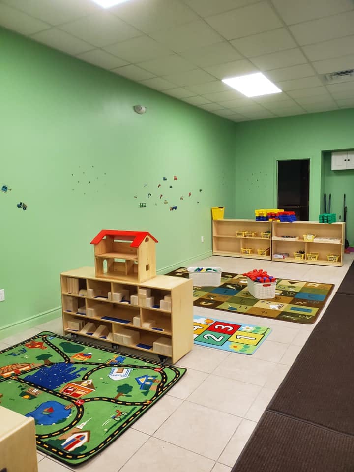 Classroom with play rugs, wooden shelves, and a dollhouse