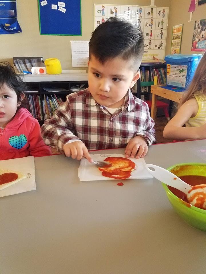 Child spreading sauce on a flatbread with a knife