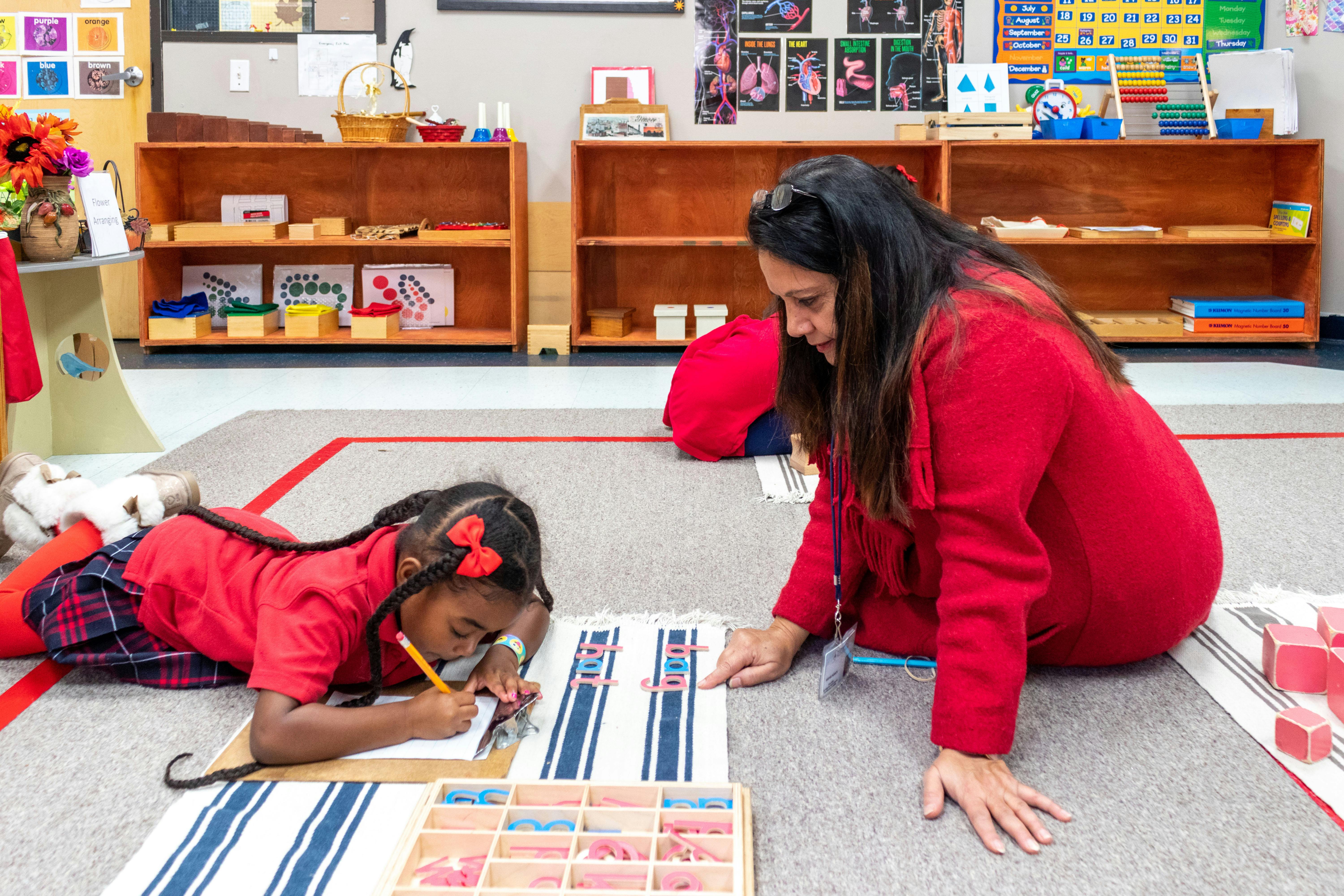 Person and child on floor working with learning materials in a classroom